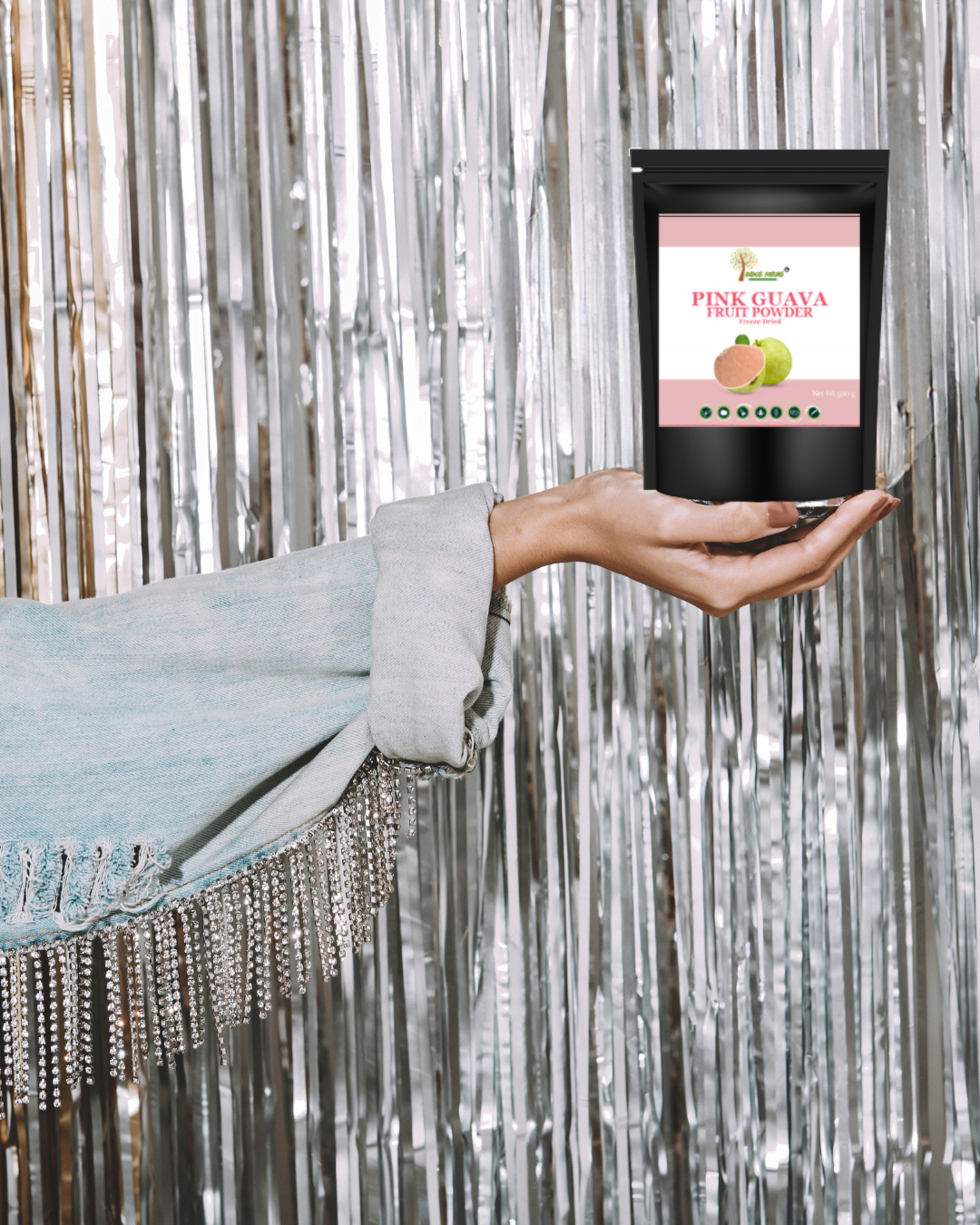 Hand holding a package of Pink Guava Fruit Powder against a silver tinsel background