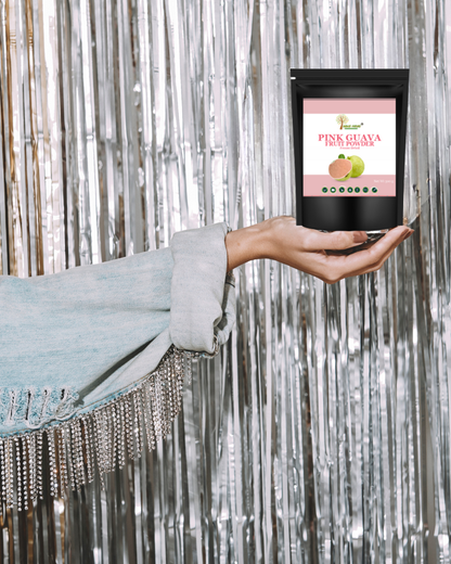 Hand holding a package of Pink Guava Fruit Powder against a silver tinsel background